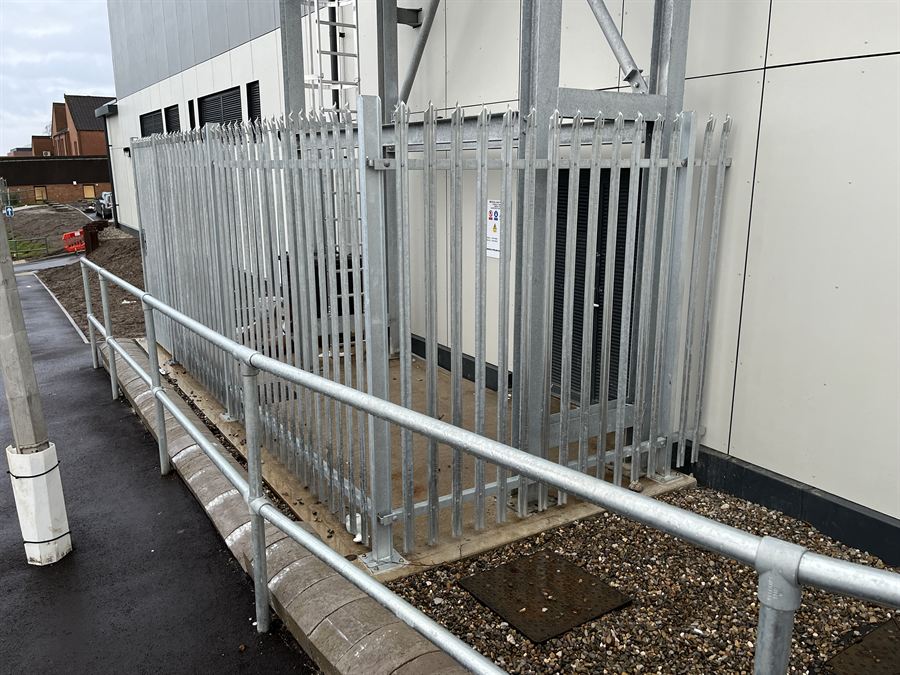 Galvanised palisade service compound alongside a tubular pedestrian handrail