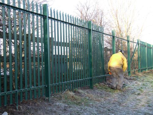 Green powder coated palisade fencing being installed around a football field perimeter