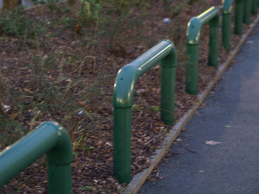 Green tubular pedestrian guardrail installed alongside a path